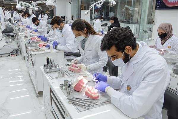“Female Pakistani Dental Technology students wearing scarves and lab coats working in a dental lab